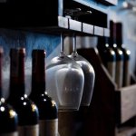 Close-up of wine bottles and glasses on wooden shelves in a dimly lit cellar, creating a cozy ambiance.