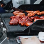 Close-up of a chef grilling various sausages on an outdoor barbecue grill, perfect for summer events.