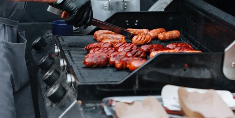 Close-up of a chef grilling various sausages on an outdoor barbecue grill, perfect for summer events.